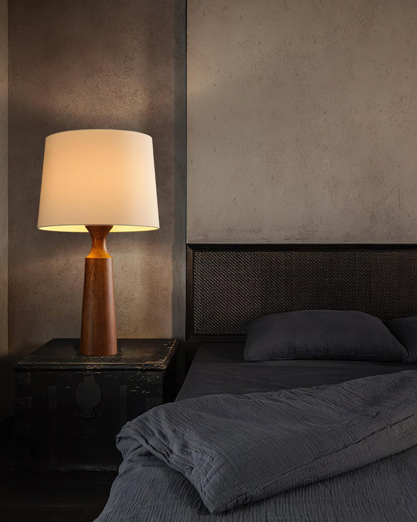 Console table lamp in walnut lit on a nightstand beside a bed