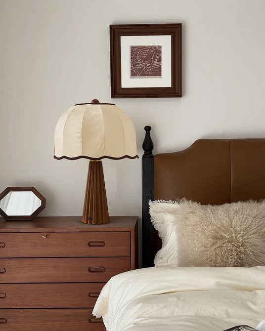 Scalloped shade lamp lit on a walnut dresser beside a made bed