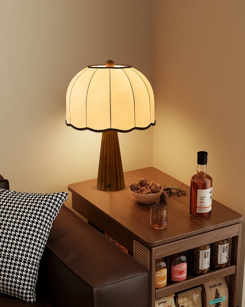 Scalloped shade lamp lit on a side table beside a bottle and a tray