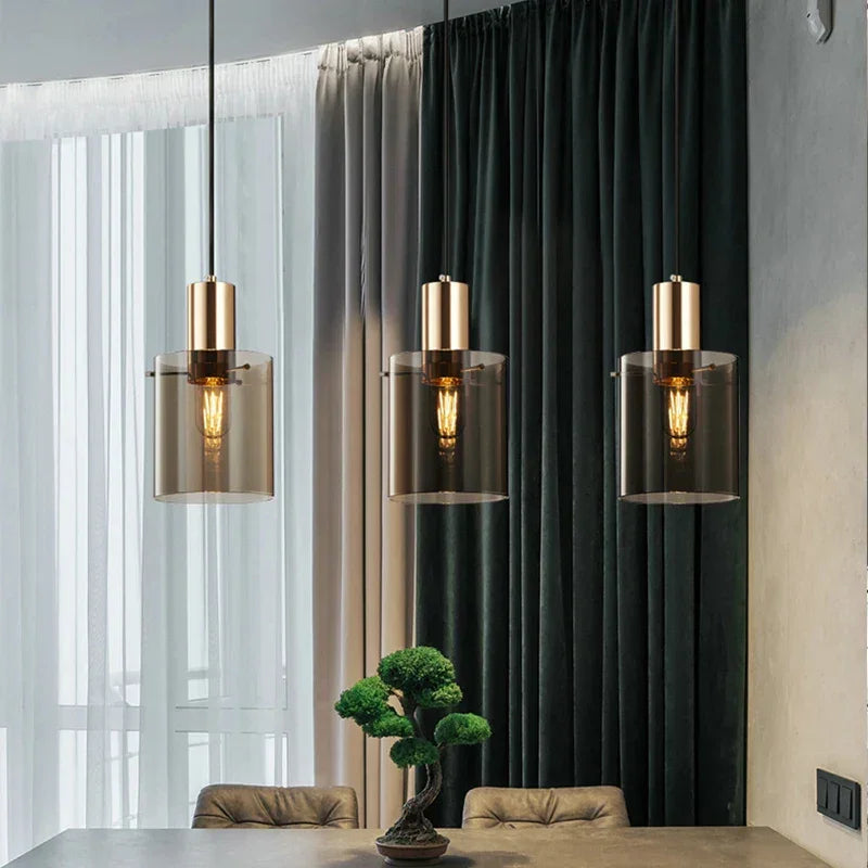 Three copper pendants in a row lit in front of a dark green curtain