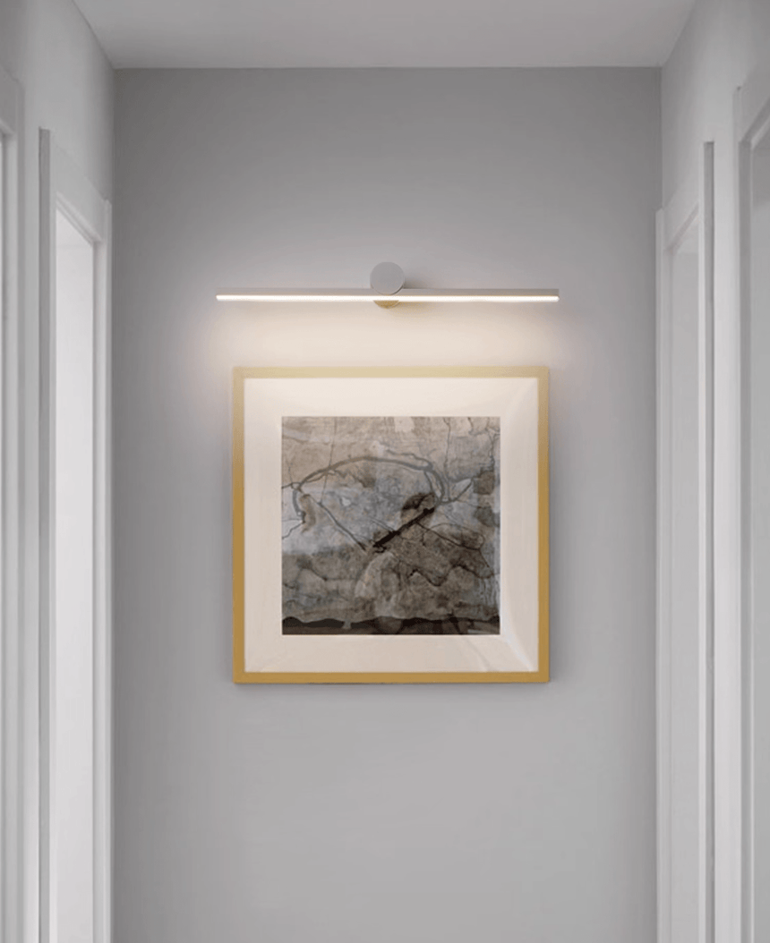 Black bar lit above a gilt framed landscape in a narrow hallway beside a doorway