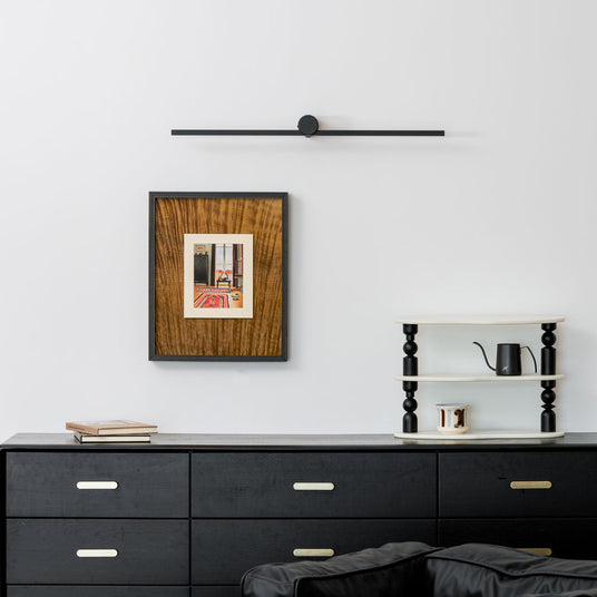Black bar lit above a framed print over a black sideboard with a kettle and books