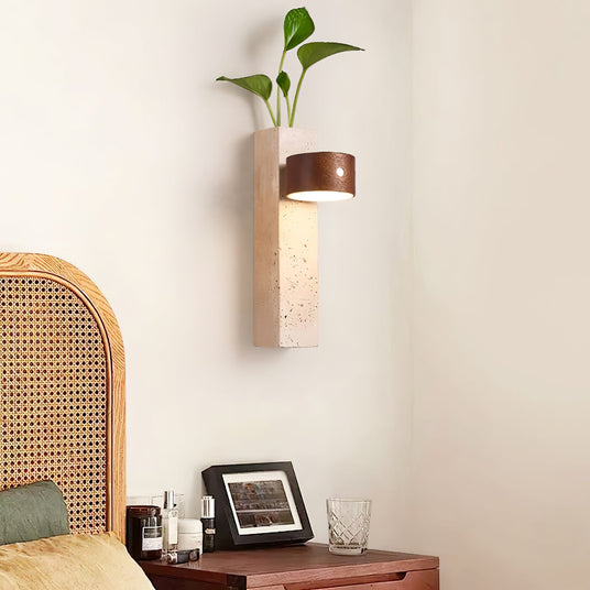 Travertine wall sconce mounted above a nightstand beside a cane headboard