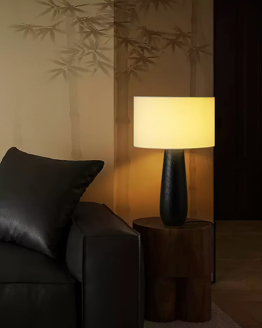 Cream table lamp lit beside a dark leather sofa and cushion