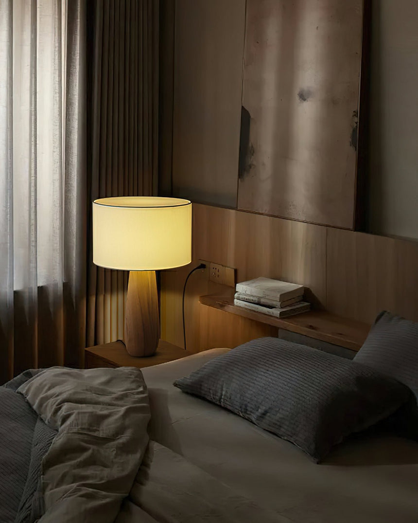 Cream table lamp lit on a bedside shelf in a dim bedroom