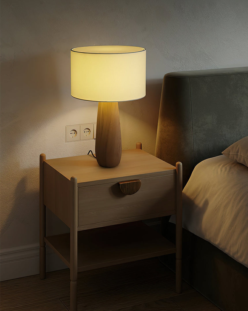 Cream table lamp lit on a nightstand against a pale wall