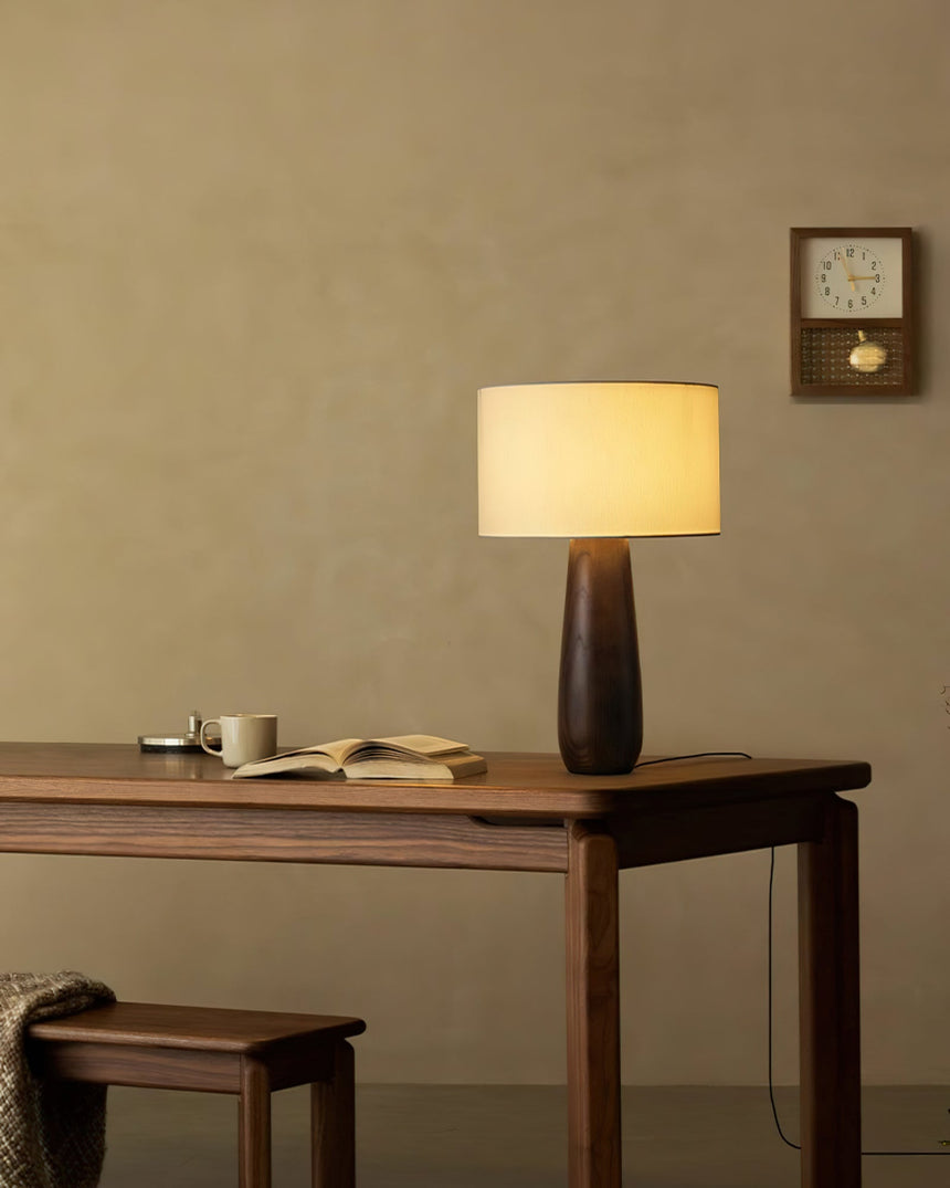 Cream table lamp lit on a wood desk beside an open notebook