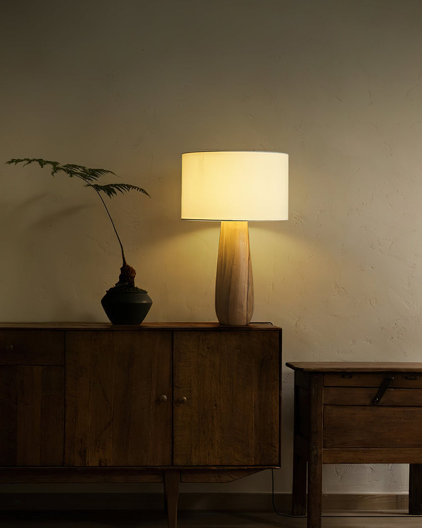 Cream table lamp lit on a sideboard beside a small dark vase