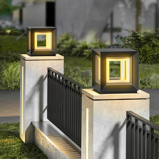 Lit cubes on pillars above a fence with a lawn and planting beyond