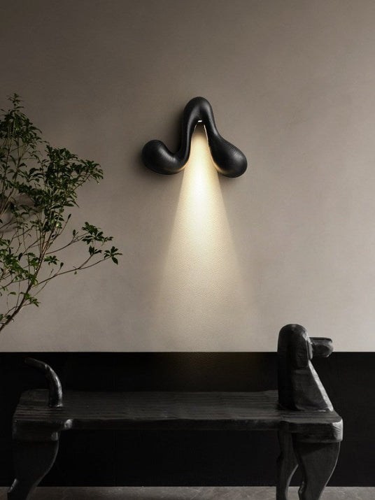 Sconce lit above a dark bench beside a branch in a tall floor vase