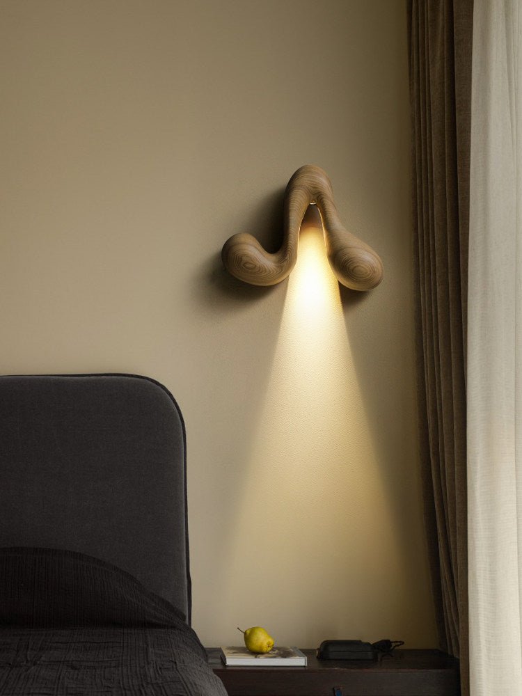 Sconce lit beside a long curtain above a headboard and a side table