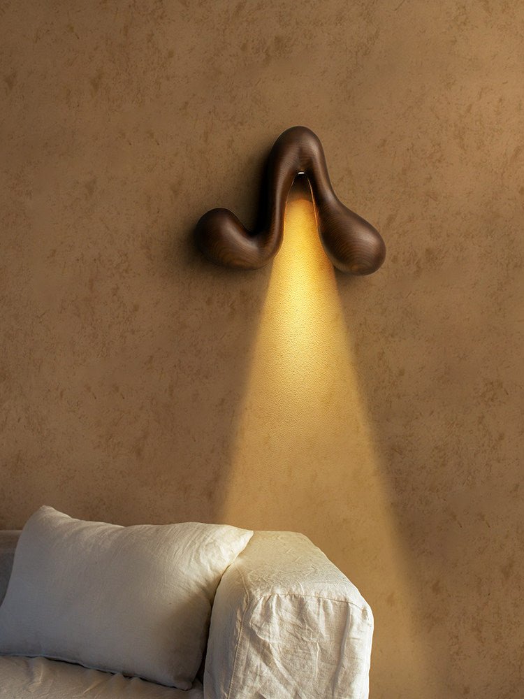 Sconce lit above a pale sofa with cushions against a plaster wall