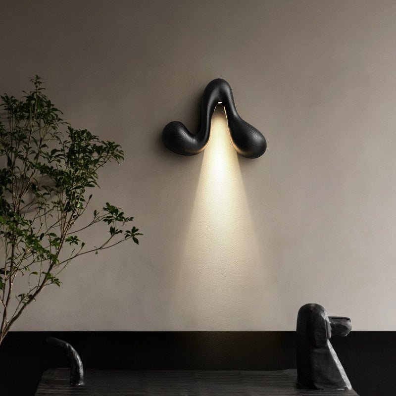 Sconce lit beside a slim plant above a dark bench in a quiet corner