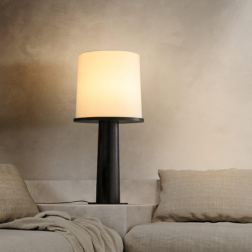Cylinder table lamp lit beside a pale sofa and a folded throw
