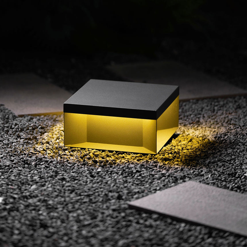 The flat box lit low on a gravel border beside a paving slab at night