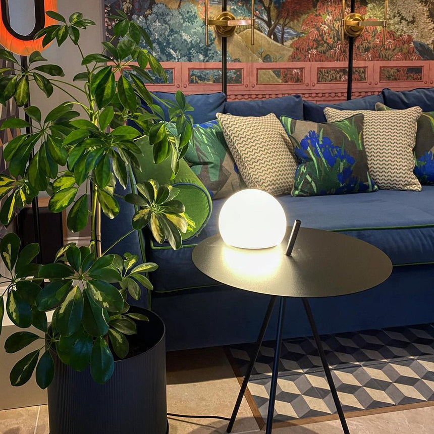 The tripod table lit beside a garden sofa with cushions and planters