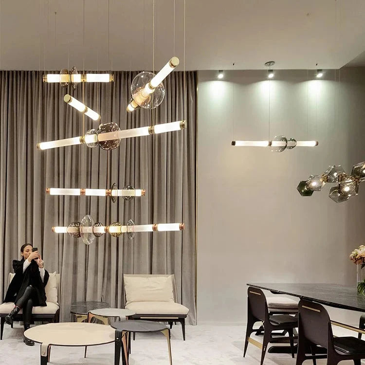Several stacked bead pendants lit in a wide room with armchairs and a bar