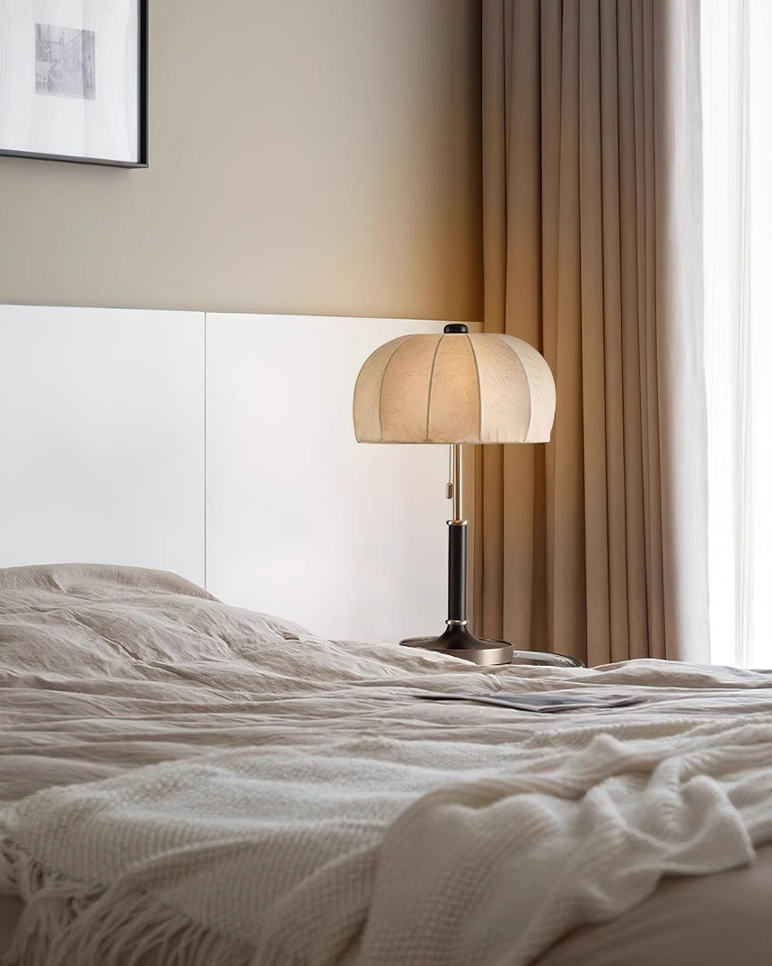 Segmented dome lamp lit on a nightstand beside a bed with white linen