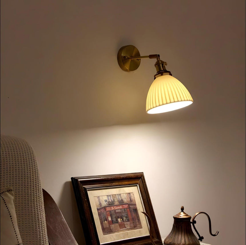 The sconce lit above a lace covered table with a framed picture and a copper kettle