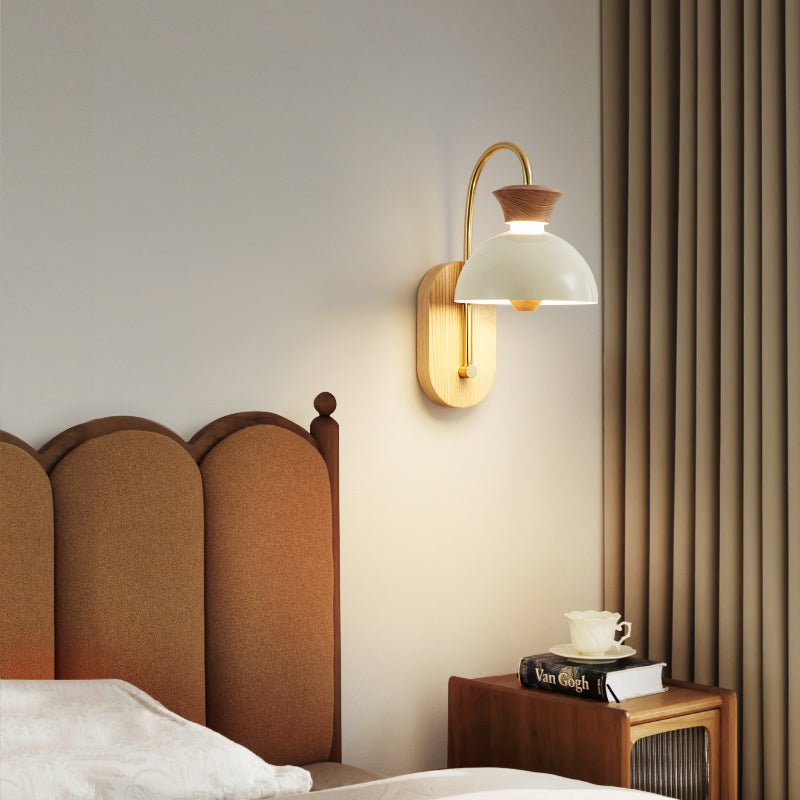 Sconce lit above a bed with an arched headboard and a cup on the nightstand