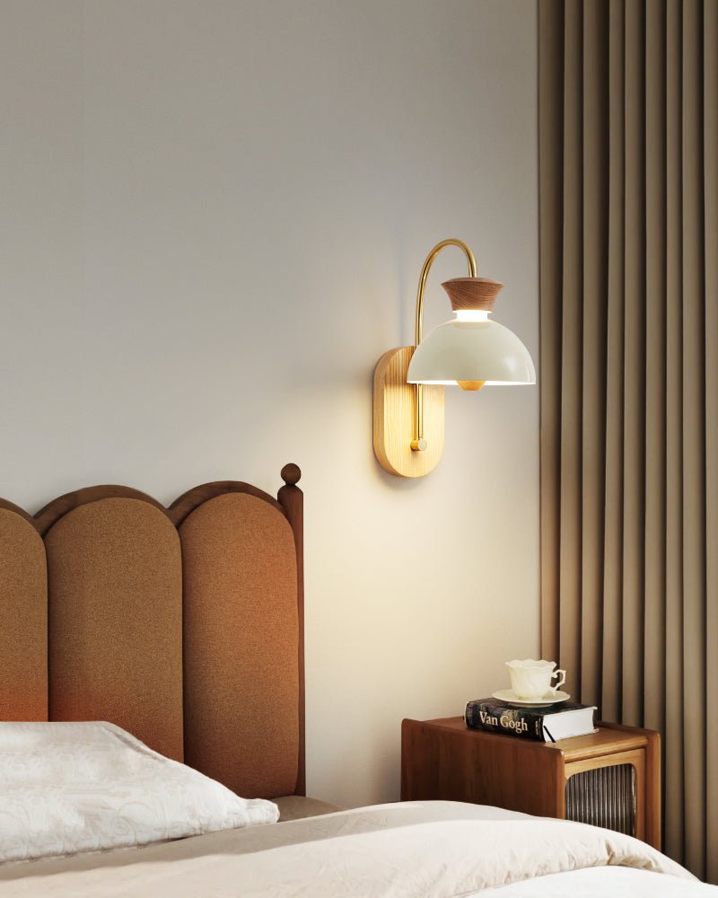 Sconce lit above an arched headboard beside a nightstand and a curtain