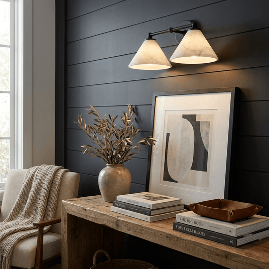 The sconce lit on a dark paneled wall above a console with framed art