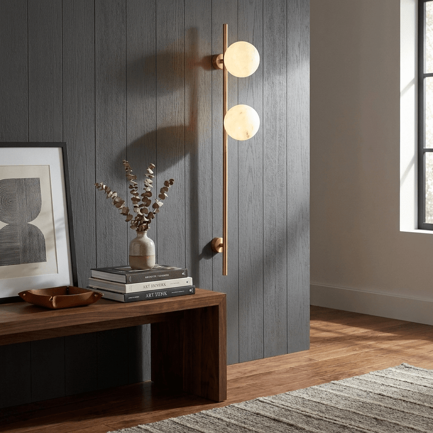 The lit sconce on a gray paneled wall above a bench with a framed print