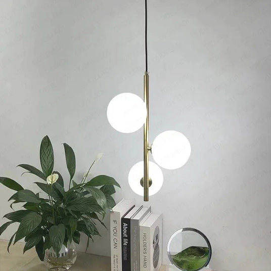 Three opal globes on brass stems above a shelf of books and a plant
