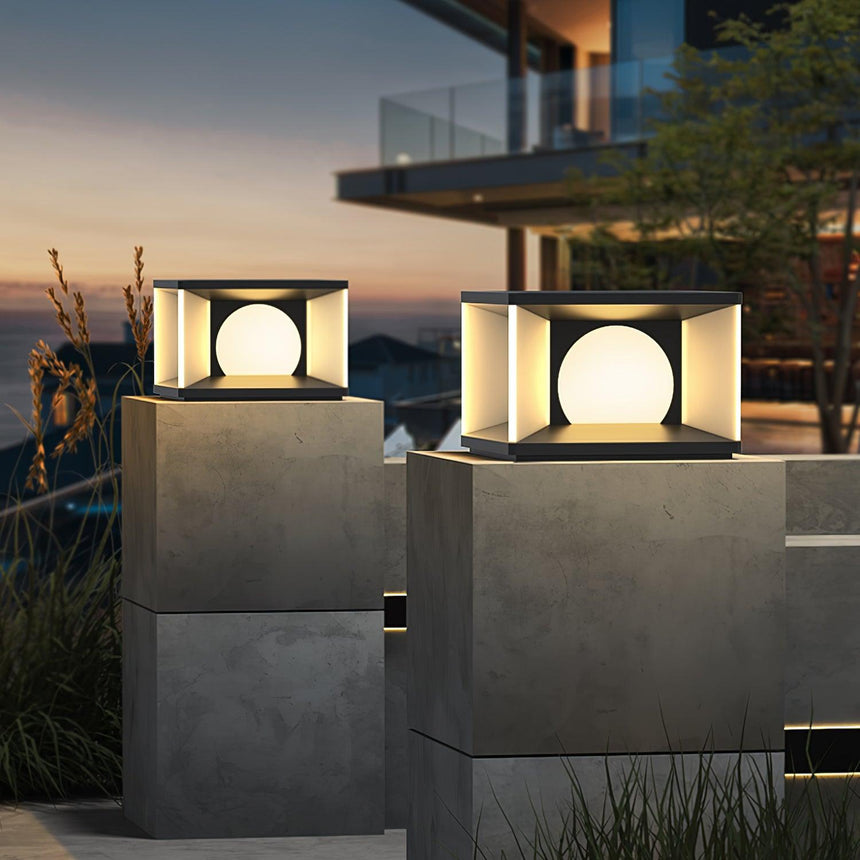 Two cubes lit on pillars below a balcony on a modern house at night