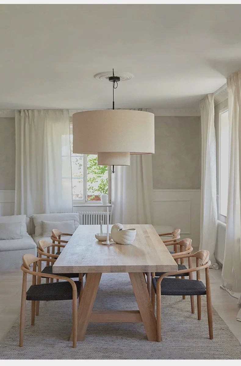 Drum shade pendant light above a dining table with woven chairs
