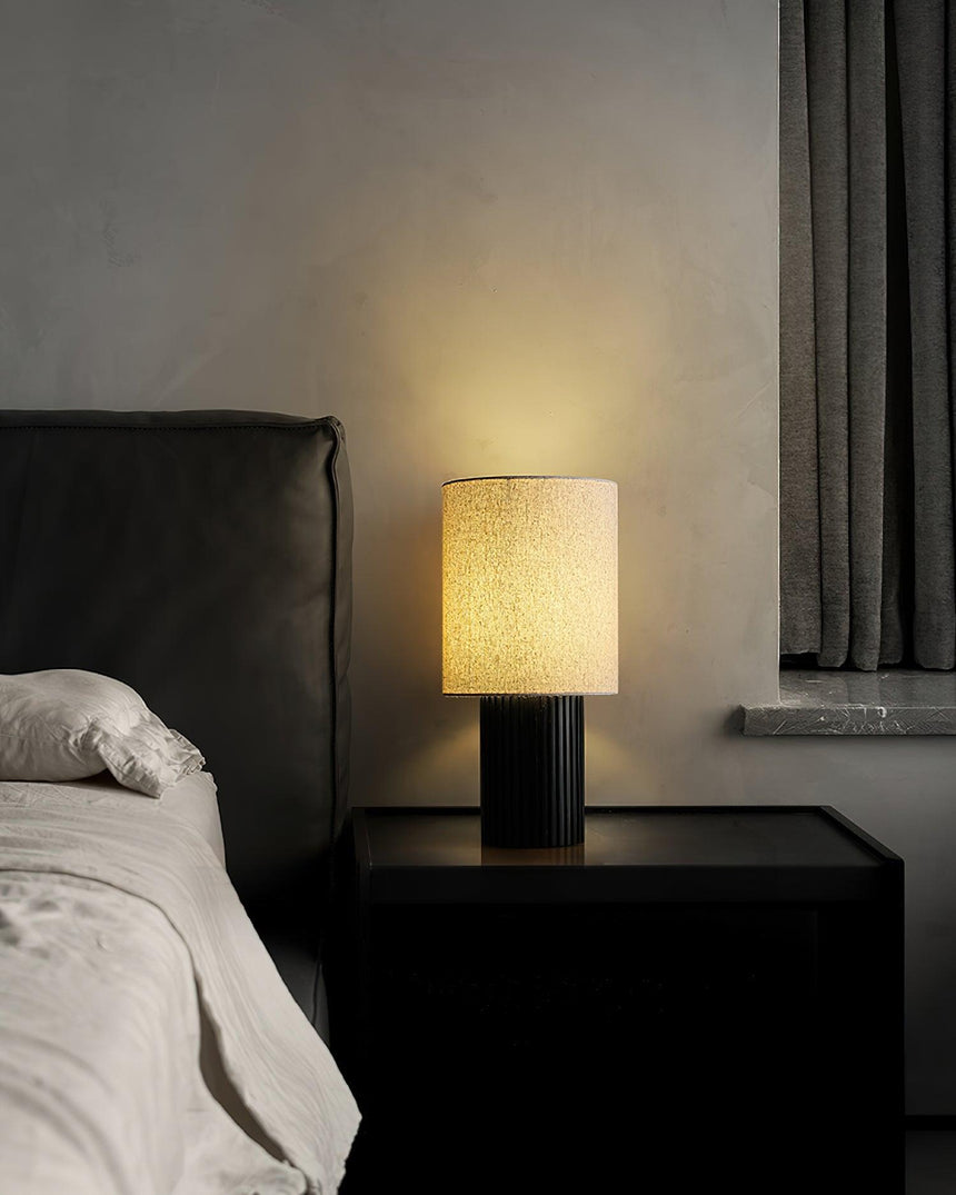 Entryway table lamp lit on a black nightstand beside a dark headboard
