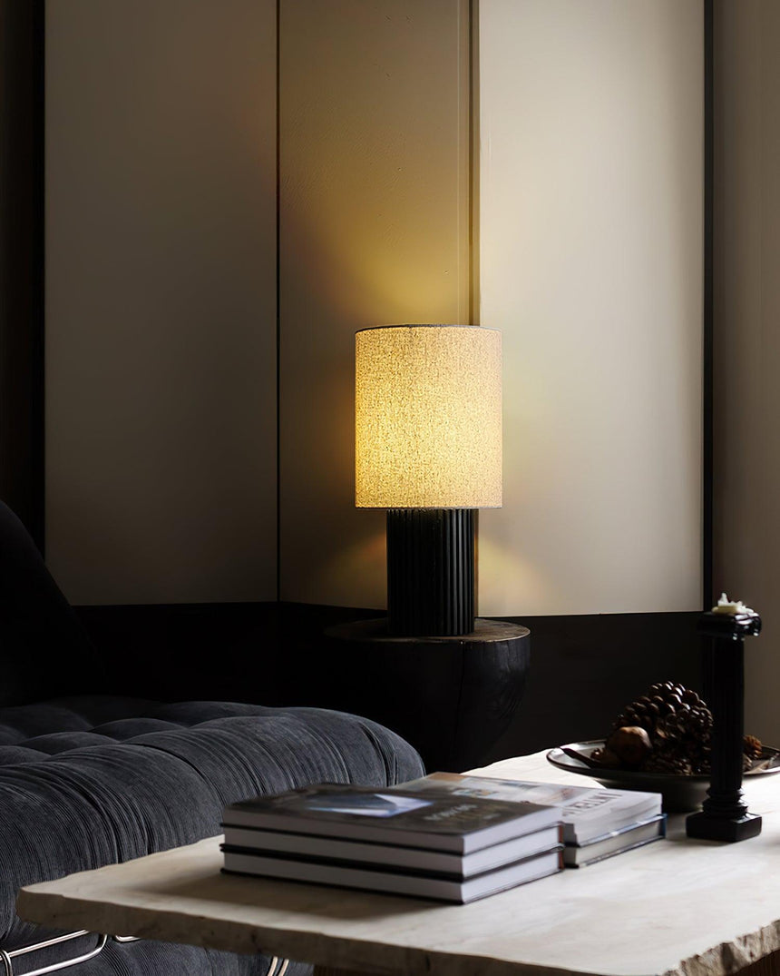 Entryway table lamp lit on a low table beside books in a dark room