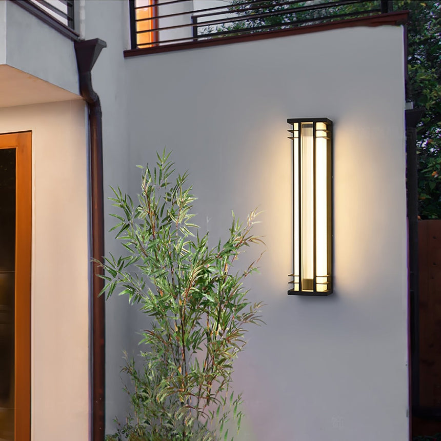 A box light lit on a rendered wall above bamboo plants beside a door