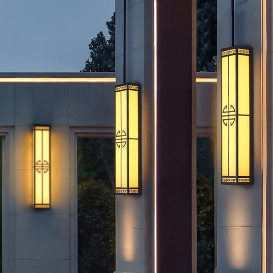 Three tall lanterns lit on facade walls beside a glass doorway at dusk