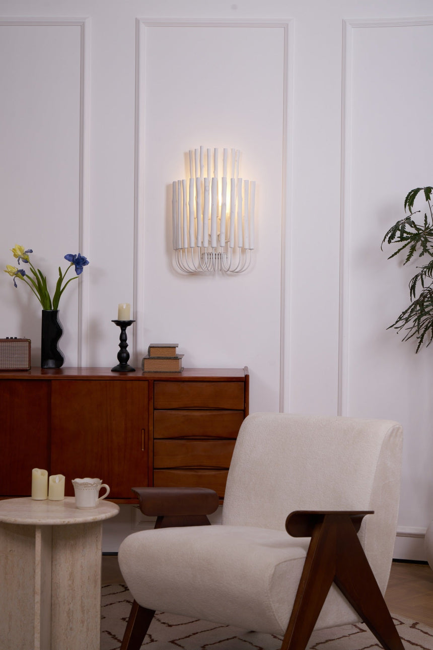 Rod sconce lit on a paneled wall across from a low armchair and table