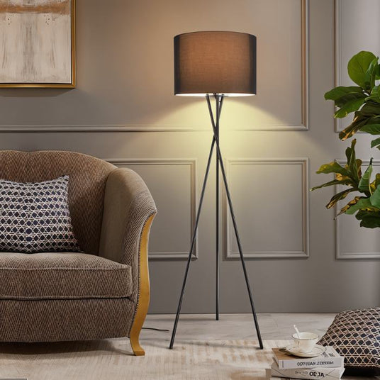 The lit lamp beside a brown armchair and a sofa in a paneled room with plants