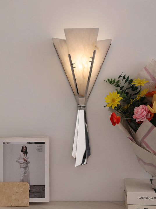 The fan sconce lit above a shelf with a framed print and colorful flowers