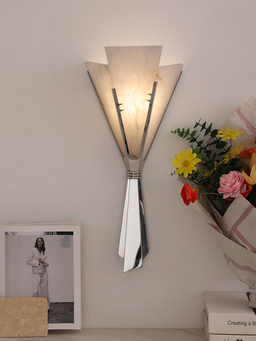The fan sconce lit above a shelf with a framed print and colorful flowers