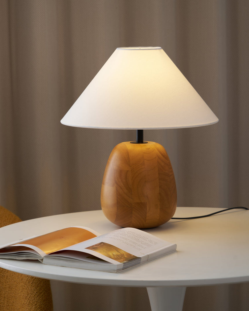 Farmhouse table lamp lit on a white round table beside an open book