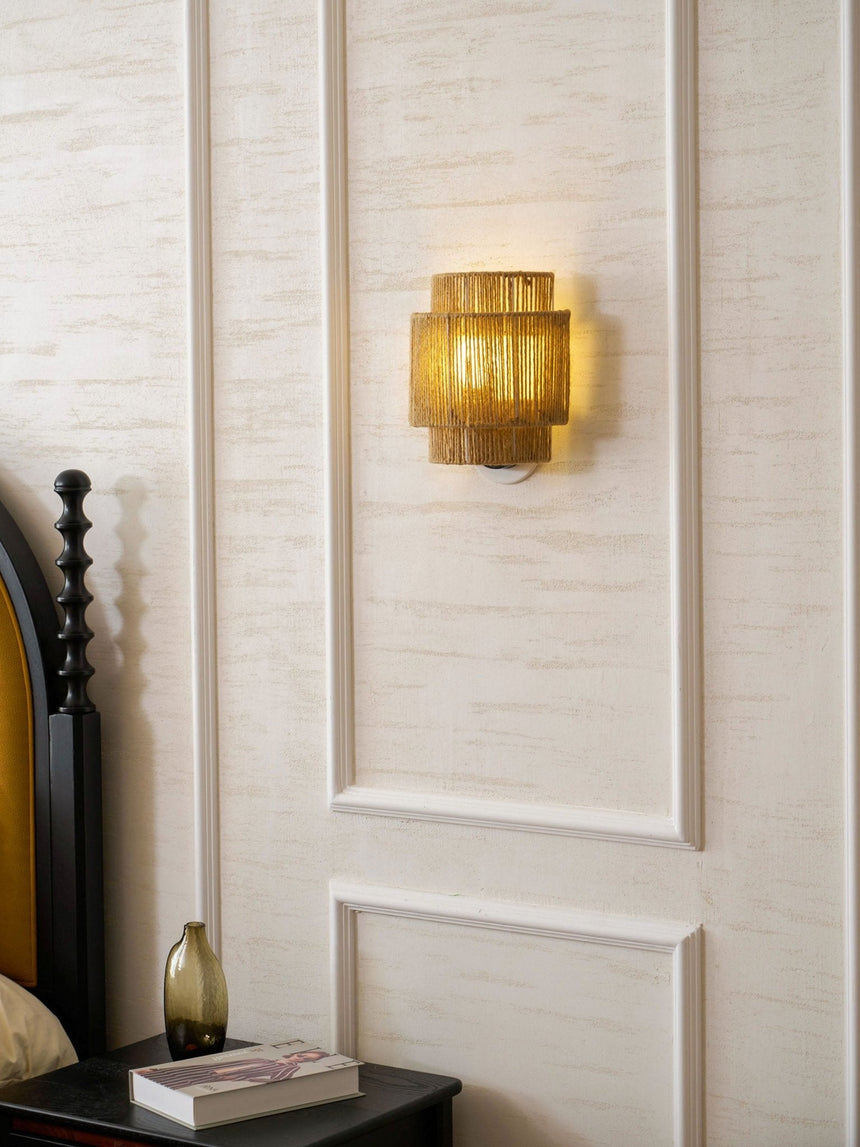 The hemp lamp lit on a paneled wall above a nightstand with a vase and books