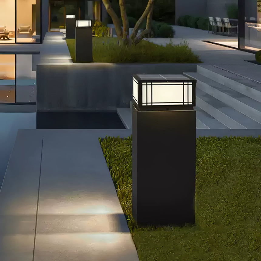 Two lanterns lit on low pillars at the edge of a lawn at night