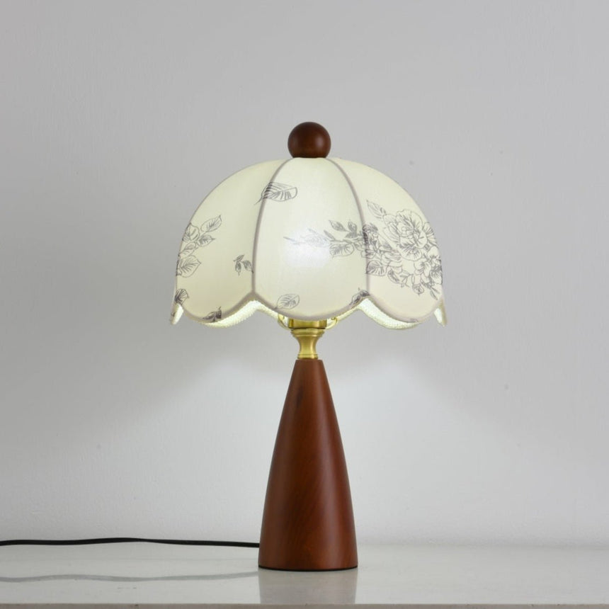 Floral table lamp lit and seen at an angle against a pale ground