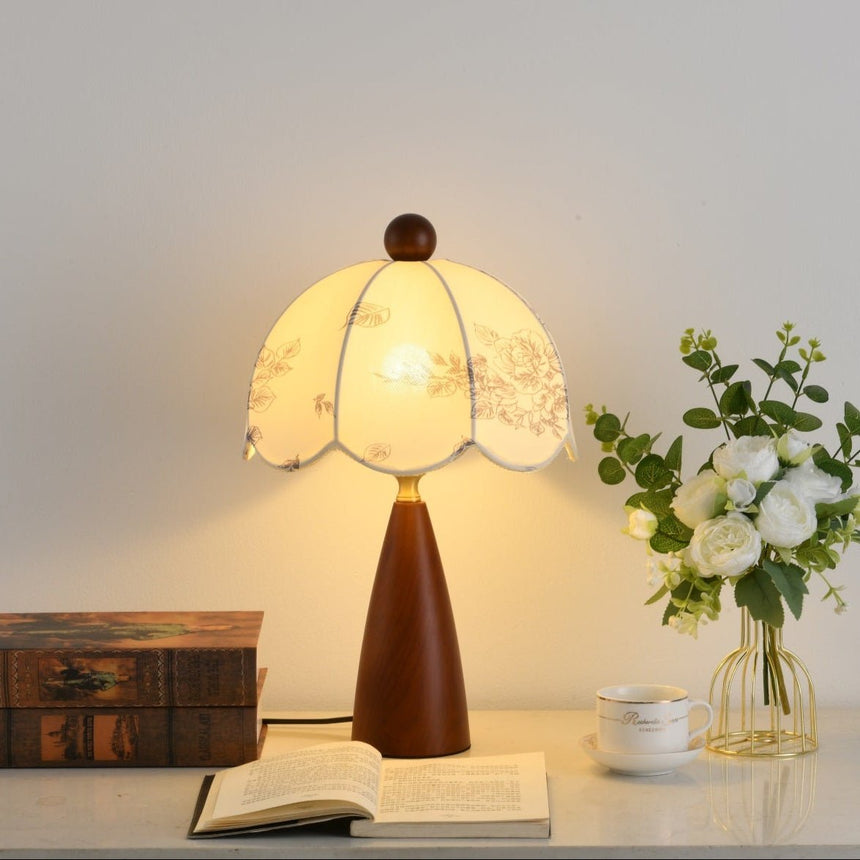 Floral table lamp lit warm on a desk beside an open book