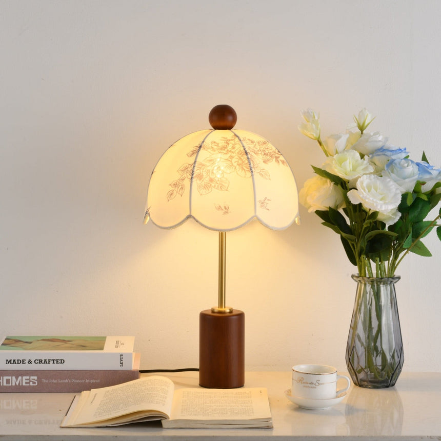 Parasol shade lamp lit beside a glass vase of cream roses