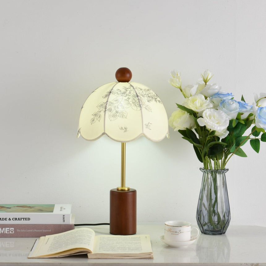 Parasol shade lamp unlit beside white roses in a glass vase