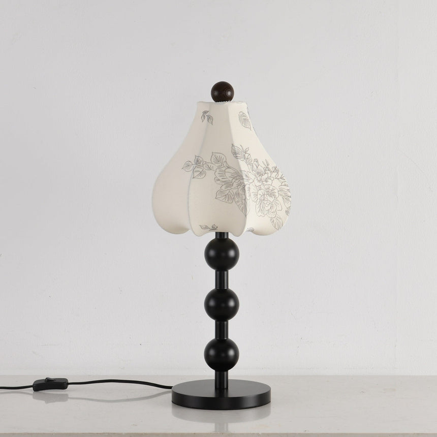 Black floral table lamp seen from an angle with the cord switch visible