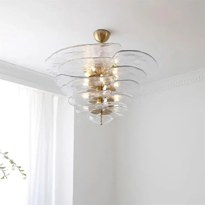 The clear glass petal shade lit under a white ceiling beside a pale curtain