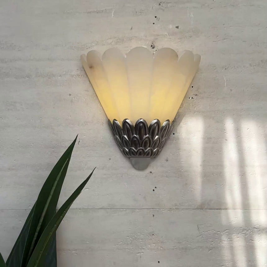 The sconce lit on a textured plaster wall beside a tall green leaf