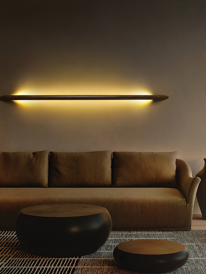 Rod lit horizontally on a warm wall above a low sofa and ottoman