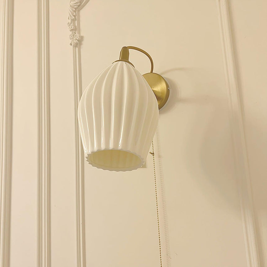The fluted shade lit on a cream paneled wall with molding